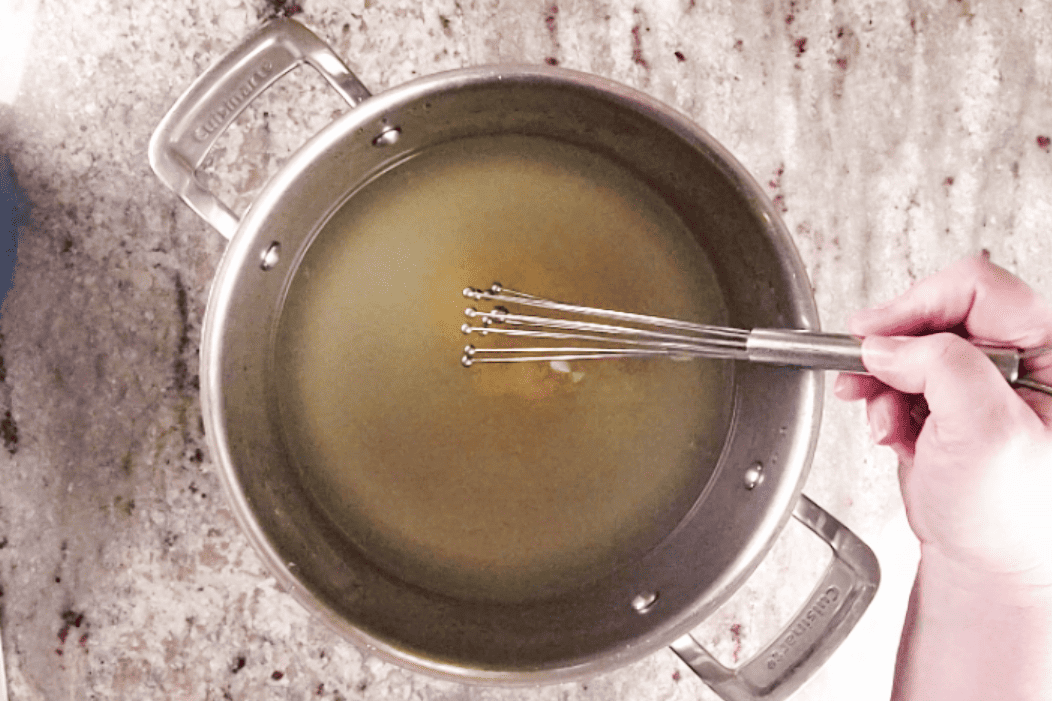 whisking chicken base into water in a soup pot